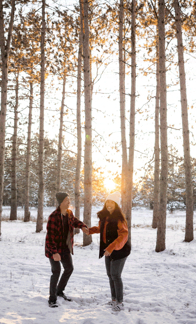 Couple jumping and cheering during their engagement session at Montissippi park in the tall pine trees.